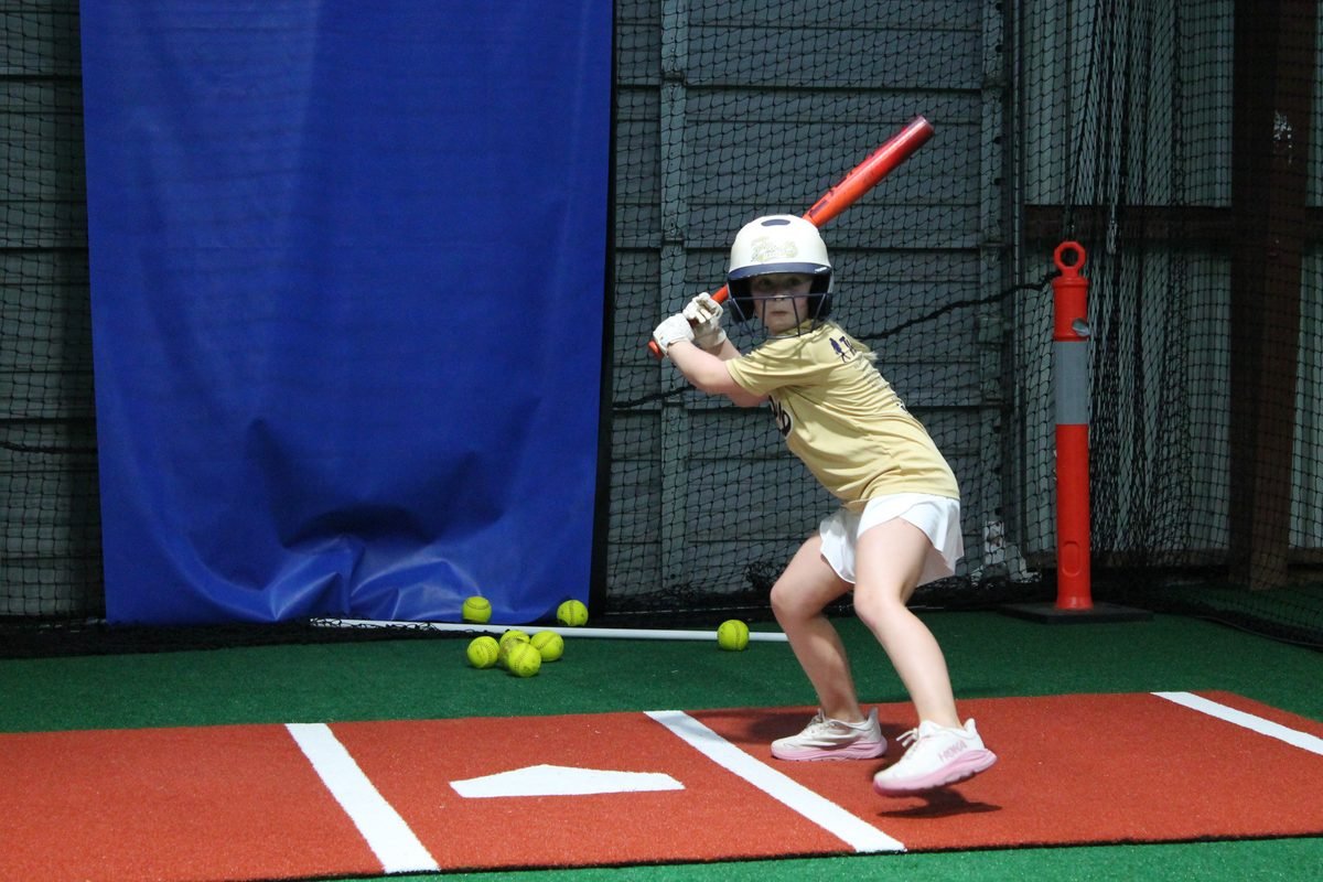 A Fury player in gold set up in her stance inside one of the batting cages