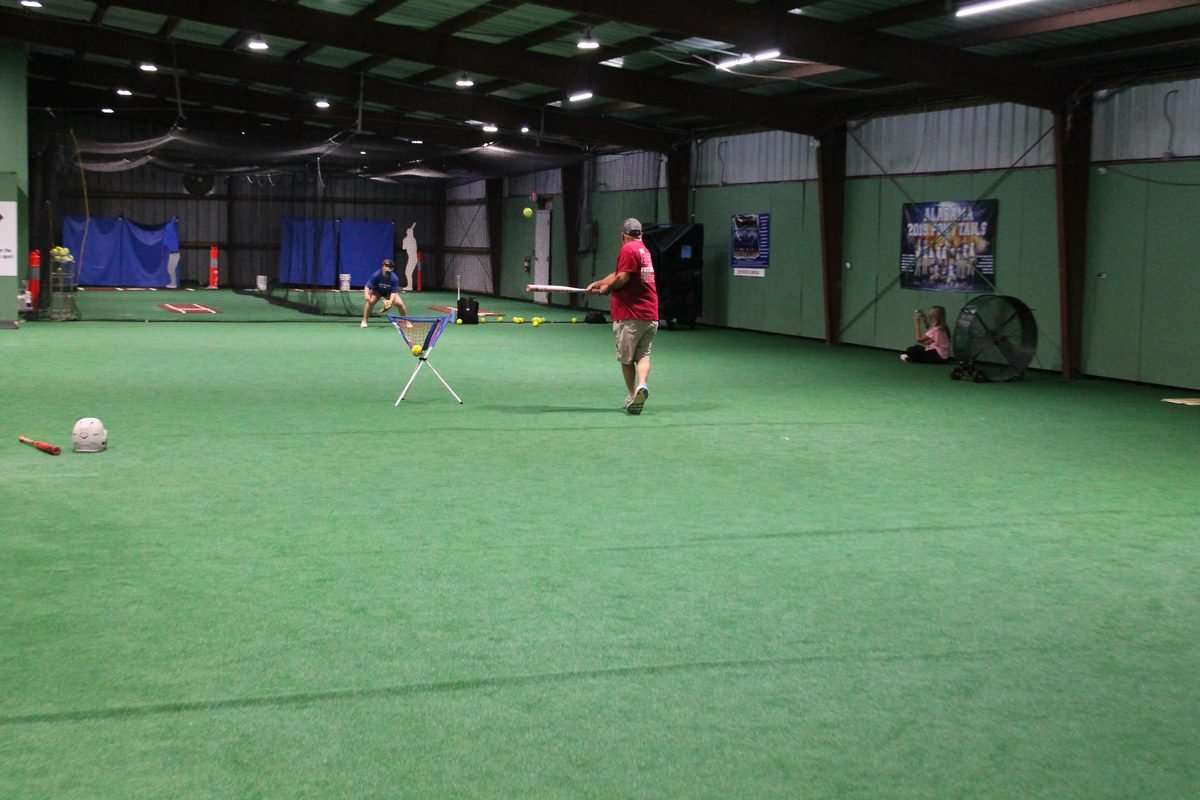 Open turf space inside the facility with a coach hitting ground balls to a fielder