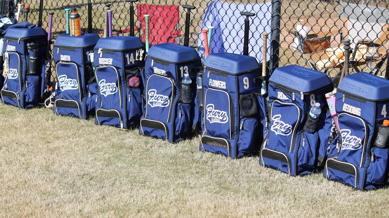 A row of navy Fury equipment bags lined up along the outfield fence